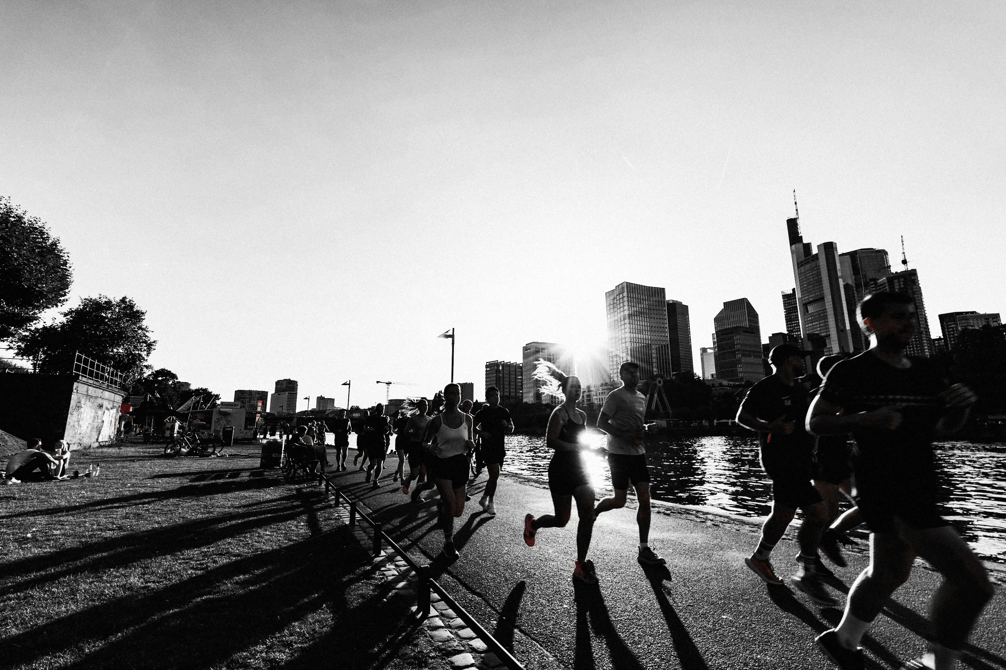 A running group on an evening run along the river in Frankfurt, the city skyline in the low sun behind them